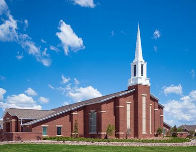 A brick church with a tall white steeple under a bright blue sky.