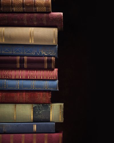 Stack of vintage books with ornate covers against dark background.