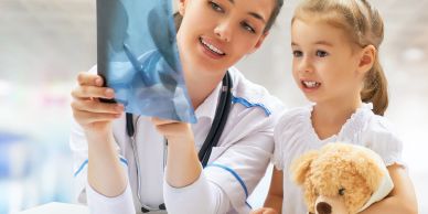 Doctor showing an X-ray to a little girl holding a teddy bear.