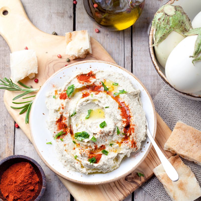 Traditional arabian eggplant dip baba ganoush with herbs and smoked paprika on a wooden background