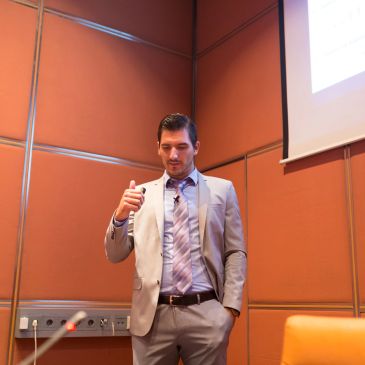 Man in a suit giving a presentation in a conference room.
