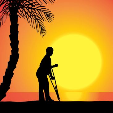 Silhouette of a person with crutches at sunset by a palm tree.