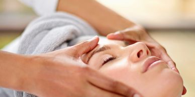A woman receives a relaxing facial massage with eyes closed.