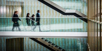 Blurred business people walk along a modern indoor walkway with patterned walls and stairs.
