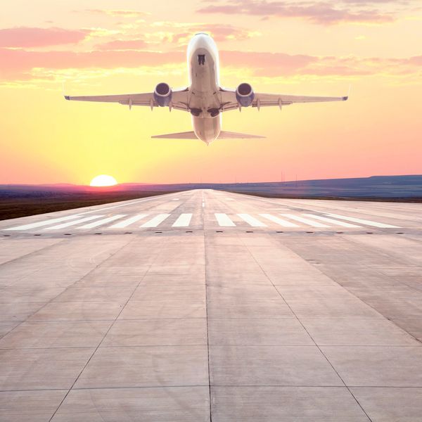 Airplane taking off from runway at sunset with vibrant sky.