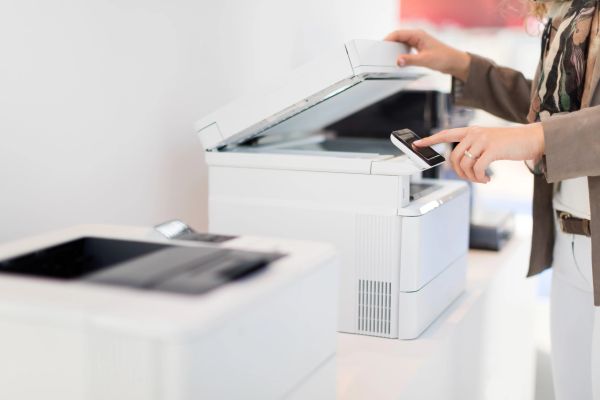Person using smartphone to operate a white office printer.