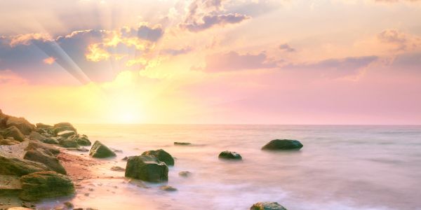 Sunset over a rocky beach with soft waves and colorful sky.