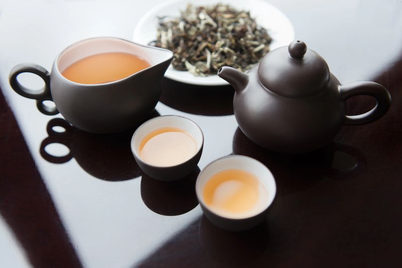 Premium white tea leaves and a traditional Chinese tea set including teapot, sharing cup and cups filled with tea for tea ceremony.