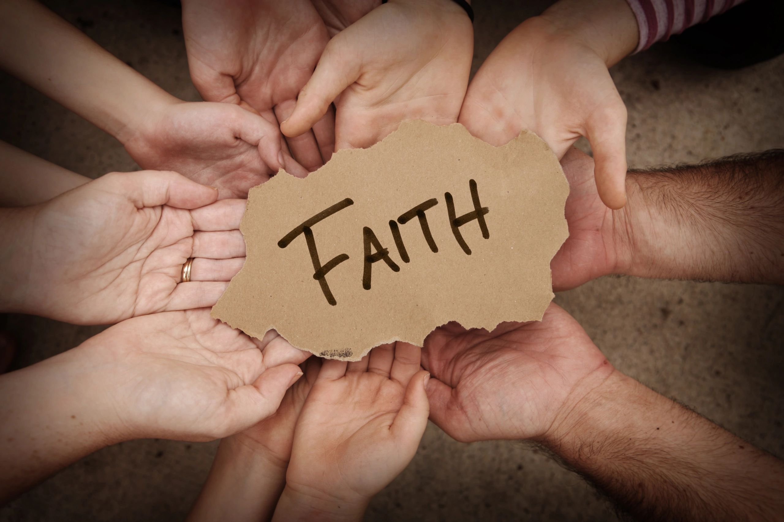 Hands holding a torn paper with 'FAITH' written on it.