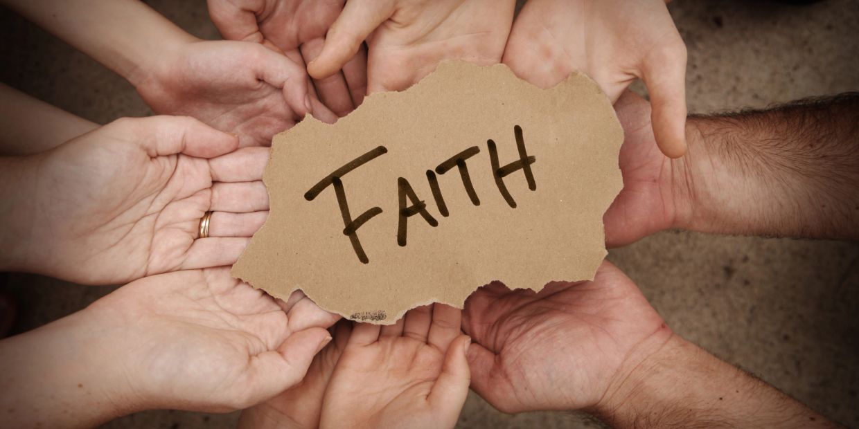 Hands holding a sign with the word 'FAITH'.