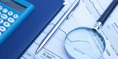 Magnifying glass, calculator, and pen on financial documents.