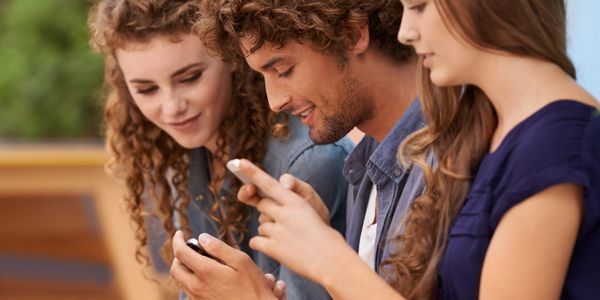 Three young people smiling and looking at their smartphones together.