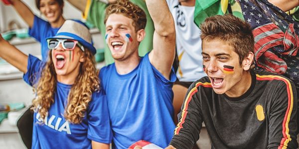 Group of enthusiastic international sports fans cheering with flags and face paint.