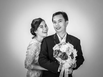 Happy couple in wedding attire posing with bouquet in black and white.