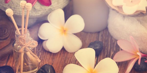 Spa setup with flowers, candles, and aromatic diffuser sticks on wooden surface.