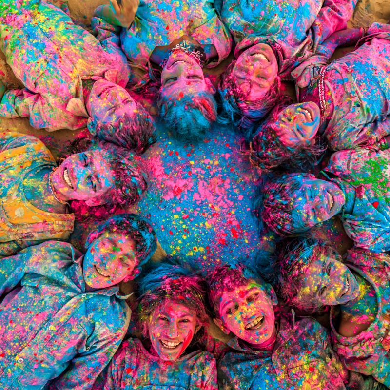 Group of happy Gypsy Indian children playing happy holi on sand dunes in desert village, Thar Desert, Rajasthan, India. Children are lying in a circle. Color powders are on their faces and clothes. Holi is a religious festival in India, celebrated, with the color powders, during the spring.