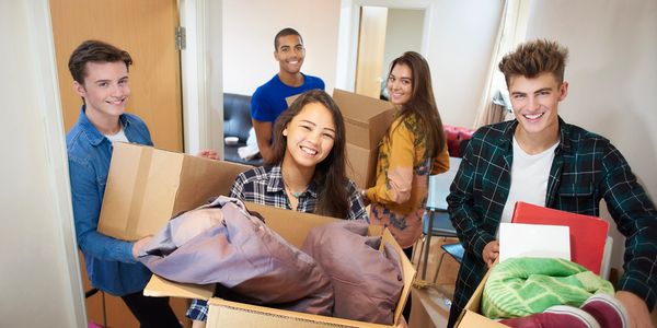 Five young adults happily moving boxes into a new home or dorm.