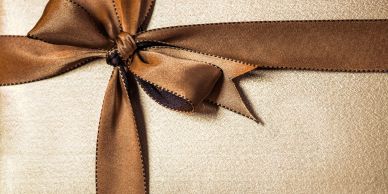 Brown ribbon tied in a bow on beige textured background.