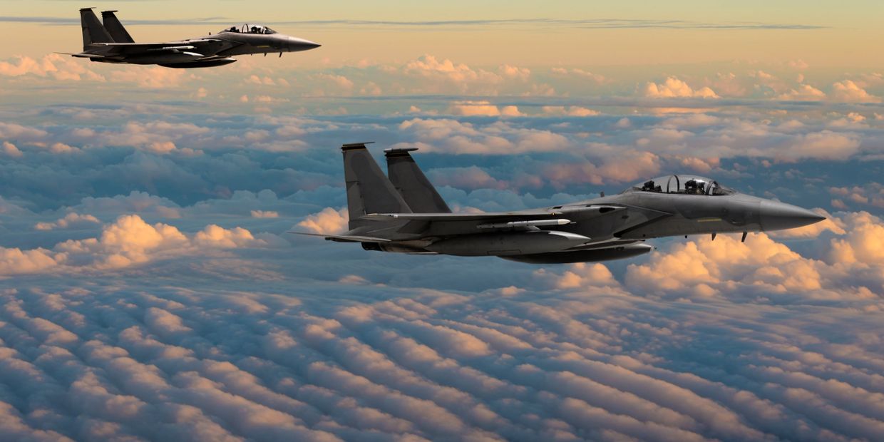 Two fighter jets flying above a sea of clouds during sunset.