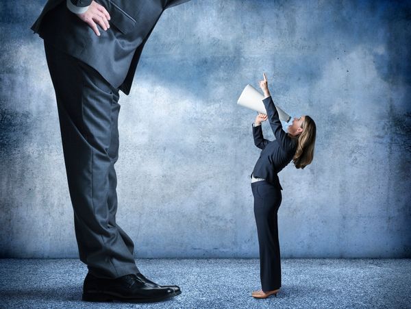 A small businesswoman shouting at a giant businessman with a megaphone.