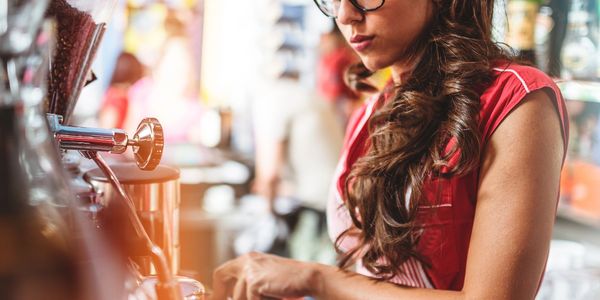 Woman with glasses making coffee at a cafe espresso machine.