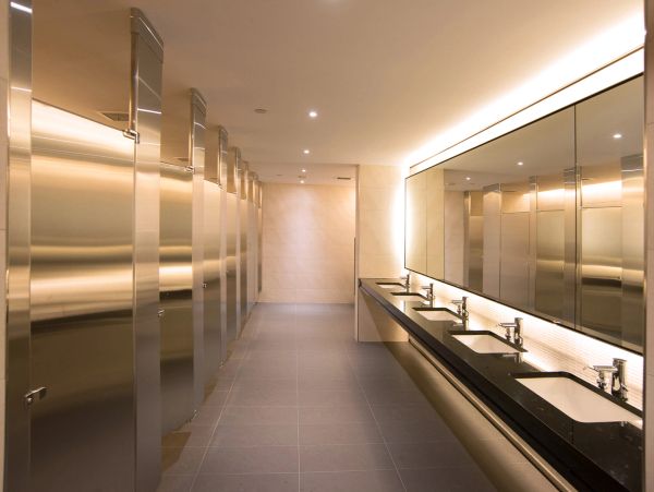 Modern public restroom with stainless steel stalls and multiple sinks.