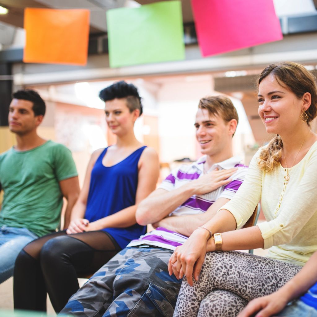 A group of young adults sitting and smiling in a casual setting.