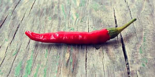 A single red chili pepper on a rustic wooden surface.