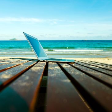 Laptop open on a wooden table by the beach.