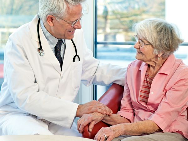 Doctor comforting elderly woman during a consultation in a bright room.