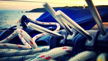 Close-up of sailing ropes and metal cleats on a boat at sunset.