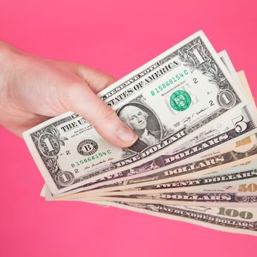 Hand holding American dollar bills against pink.