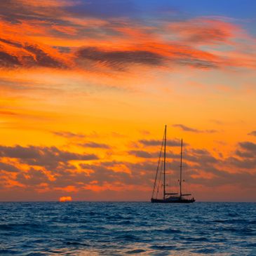 Sailboat silhouetted against a vibrant orange sunset over the ocean.