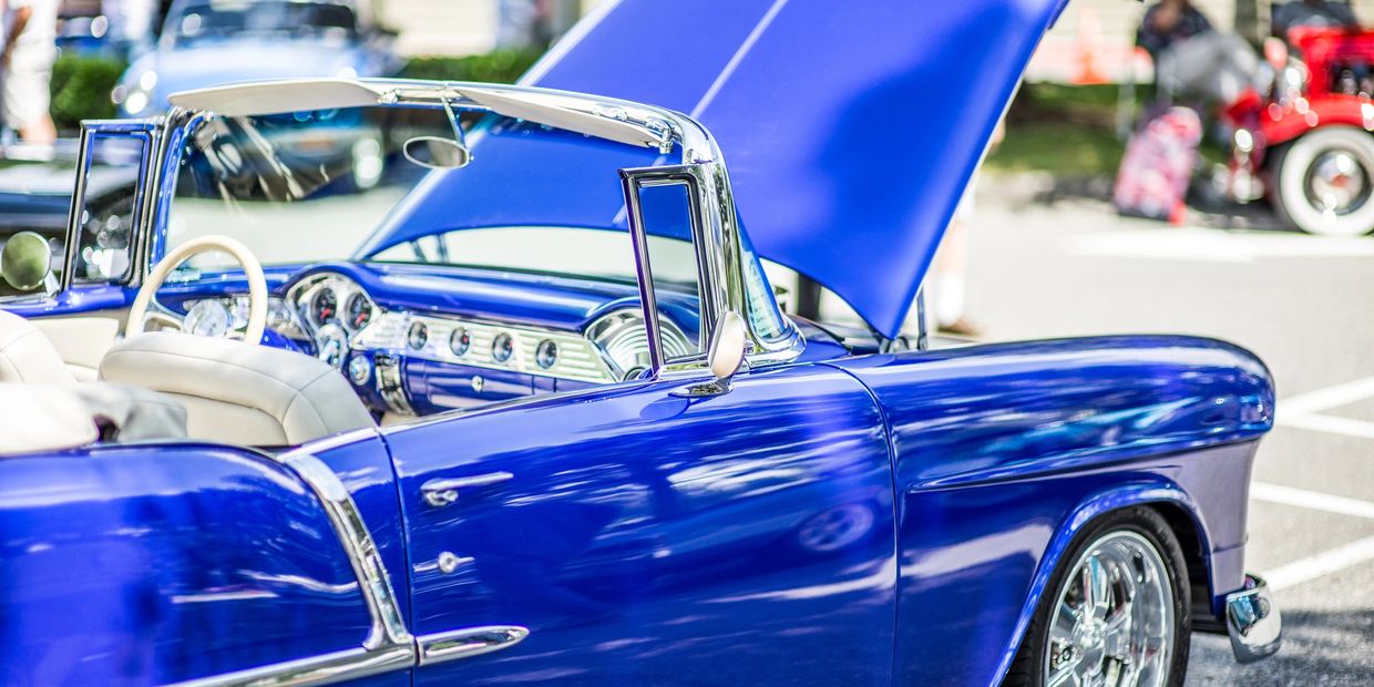 Shiny blue classic convertible car with open hood at a car show.