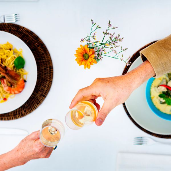 Two people toasting with white wine over a table with seafood pasta dishes.