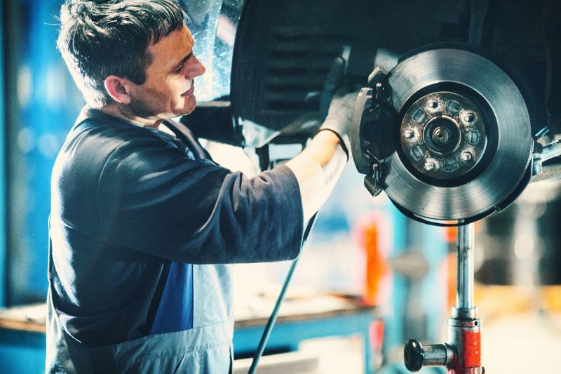 Closeup of mid aged male mechanical replacing worn out brake pads on a vehicle. The wheel has been removed and the car is lifted up on a jack. Visible braking disc. Side view.