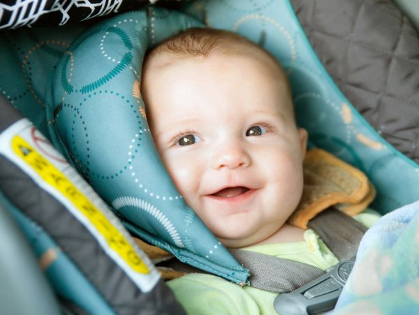 Happy baby secured in a car seat with patterned padding.