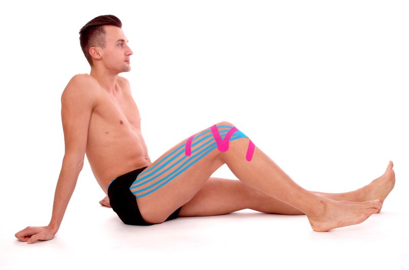 Athlete relaxed sitting on floor, Kinesiology tape on knee and on the quadriceps. Side View point and white background
