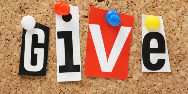 Colorful pins hold letters spelling 'GIVE' on a corkboard.