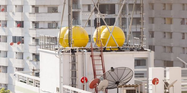 Yellow water tanks and satellite dishes on a rooftop with surrounding buildings.