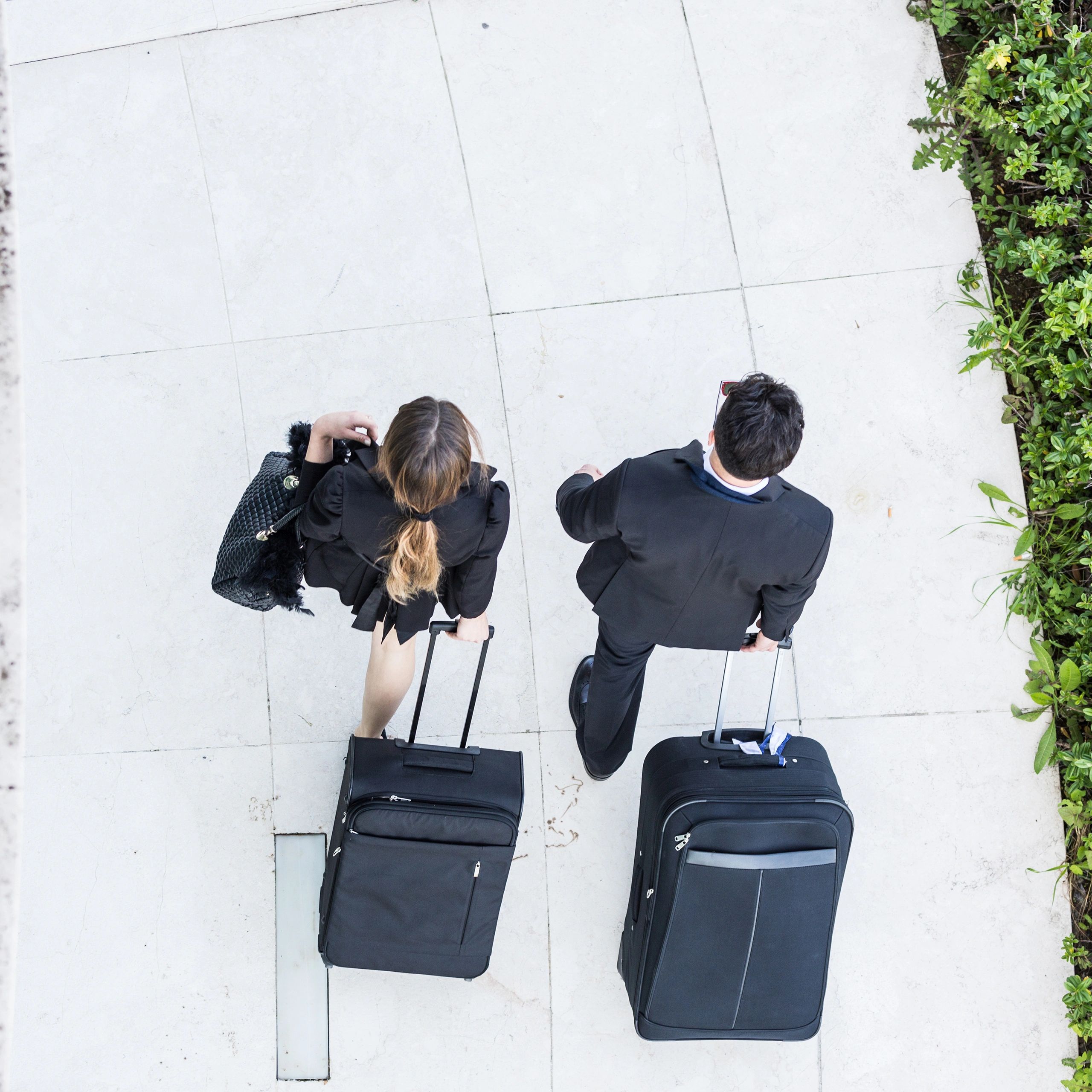 Two business travelers walking with black suitcases on a tiled floor.