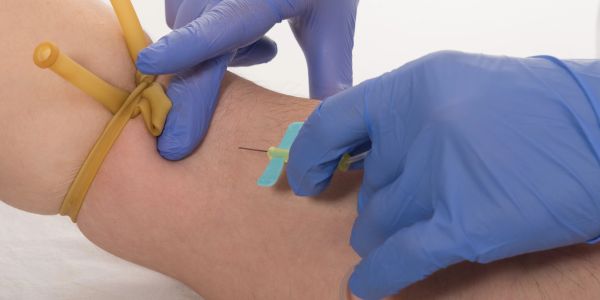Healthcare professional preparing to insert a needle into a patient's arm with a tourniquet applied.