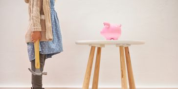 Person holding a hammer standing near a table with a pink piggy bank.