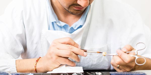 A man carefully painting a small object with a brush in a lab-like setting.