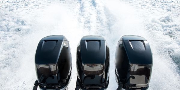 Three black outboard boat motors on water.