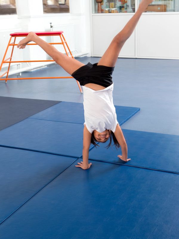 Girl doing a handstand on blue gym mats.