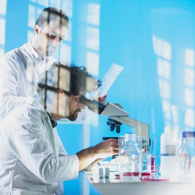 Scientists in lab coats working with a microscope and lab equipment.