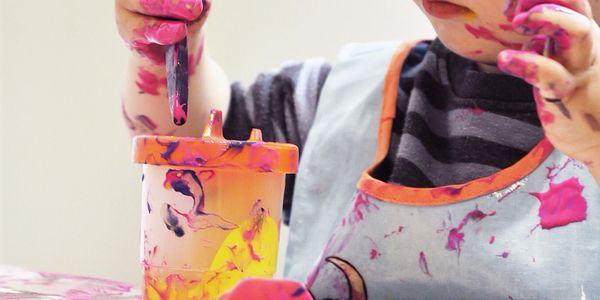 Young child focused on painting with colorful paint on hands and apron.