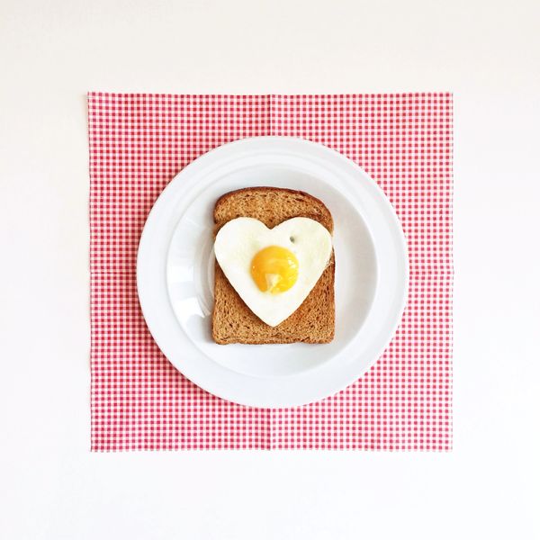 Heart-shaped fried egg on toast, served on a white plate with a red checkered napkin.
