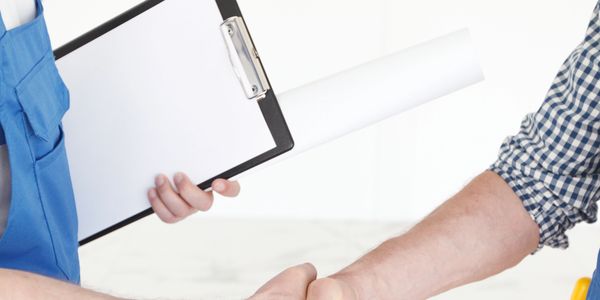 Two people shaking hands, one holding a clipboard and rolled paper.
